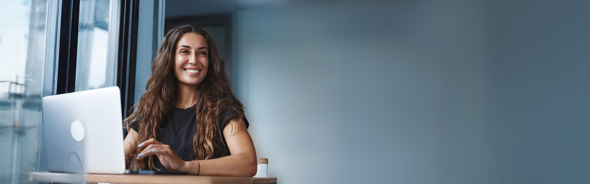 Junge Frau im Büro sitzt lächelnd vor ihrem Laptop