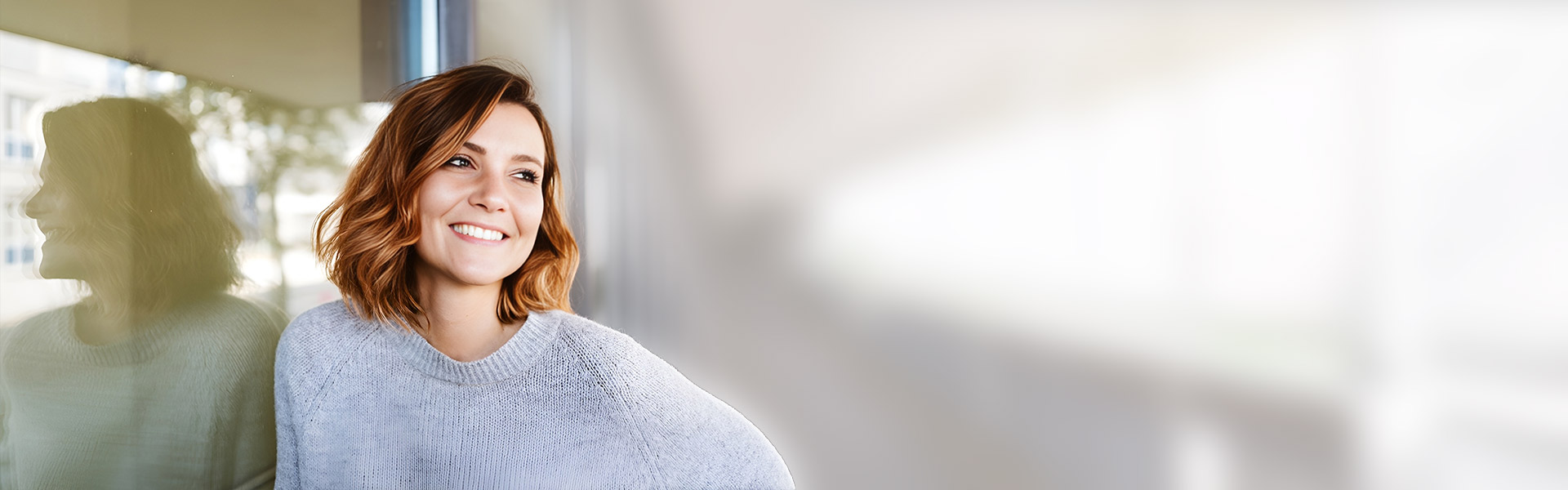eine rothaarige Frau lehnt an der Wand und lächelt