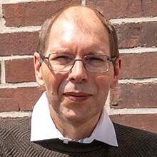 Der erfolgreiche Umschüler André Pardun steht mit verschränkten Armen vor einer geziegelten Hauswand.