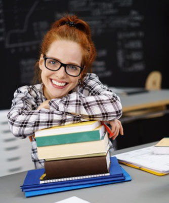 ein Mädchen sitzt an einem Schreibtisch mit Büchern und einer Tafel im Hintergrund