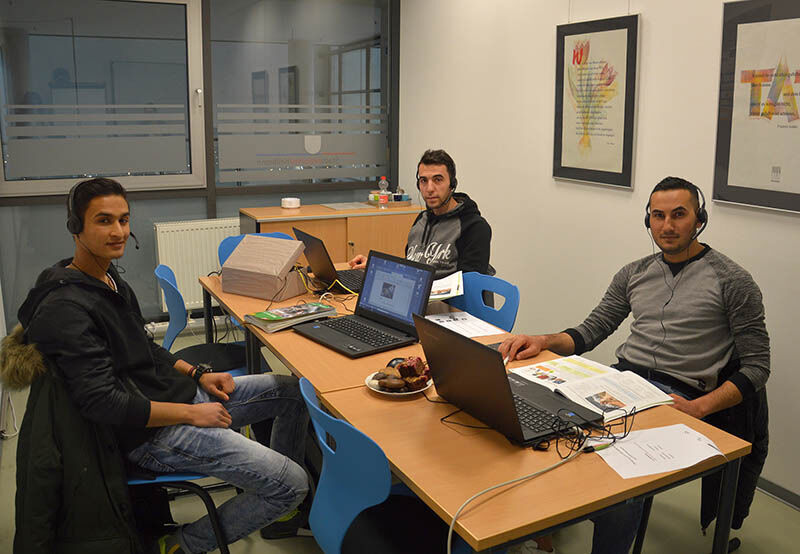 drei Männer sitzen an einem Tisch mit Laptops