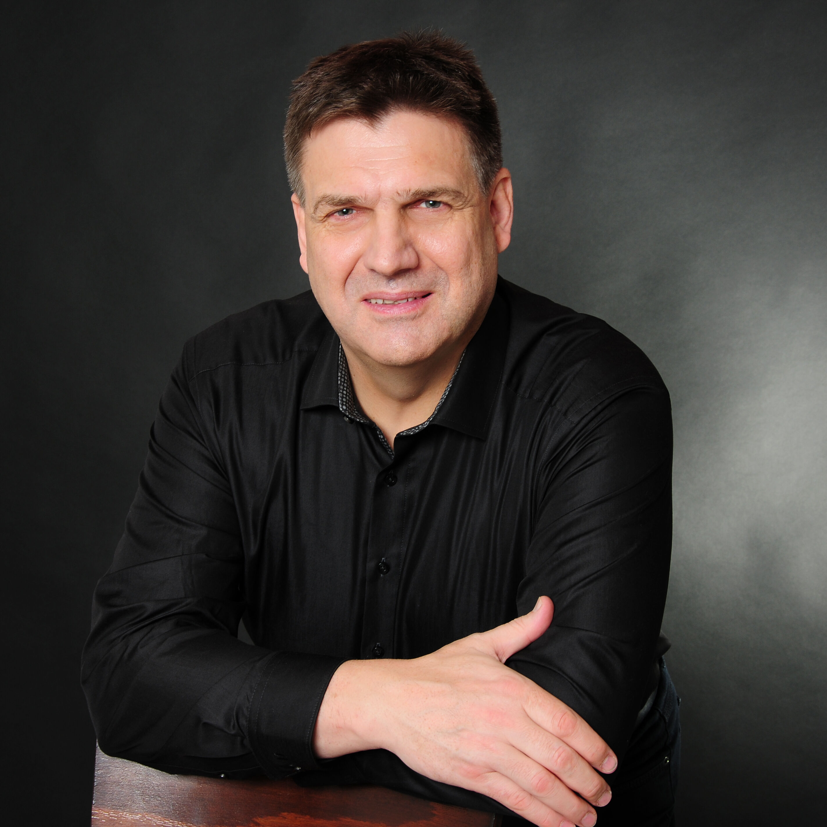 Professionelles Foto von Peter Jähne, Lernzeitbegleitung beim IBB, in dunklem Hemd vor dunklem Hintergrund.